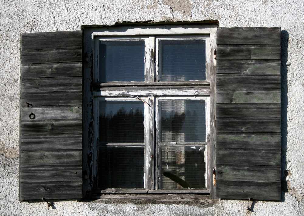 Fenêtre à volets grisâtres sur façade de ciment, quatre vitres divisées en deux étages