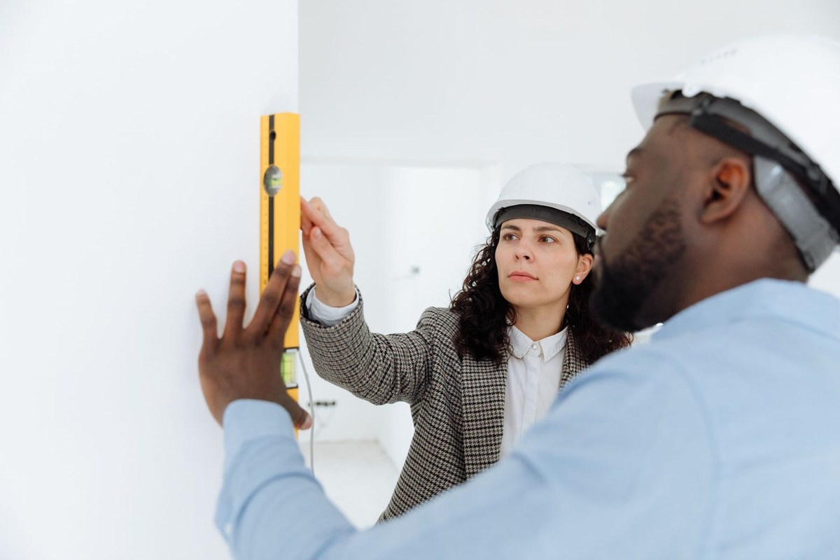 Professionnels en casques vérifient l'alignement d'un niveau sur un mur Professionnels en casques vérifient l'alignement d'un niveau sur un mur