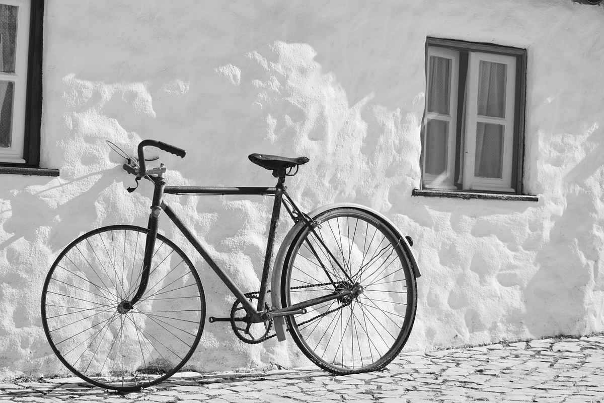Vélo noir accoudé contre un mur blanc de bâtiment ancien avec fenêtres Vélo noir accoudé contre un mur blanc de bâtiment ancien avec fenêtres