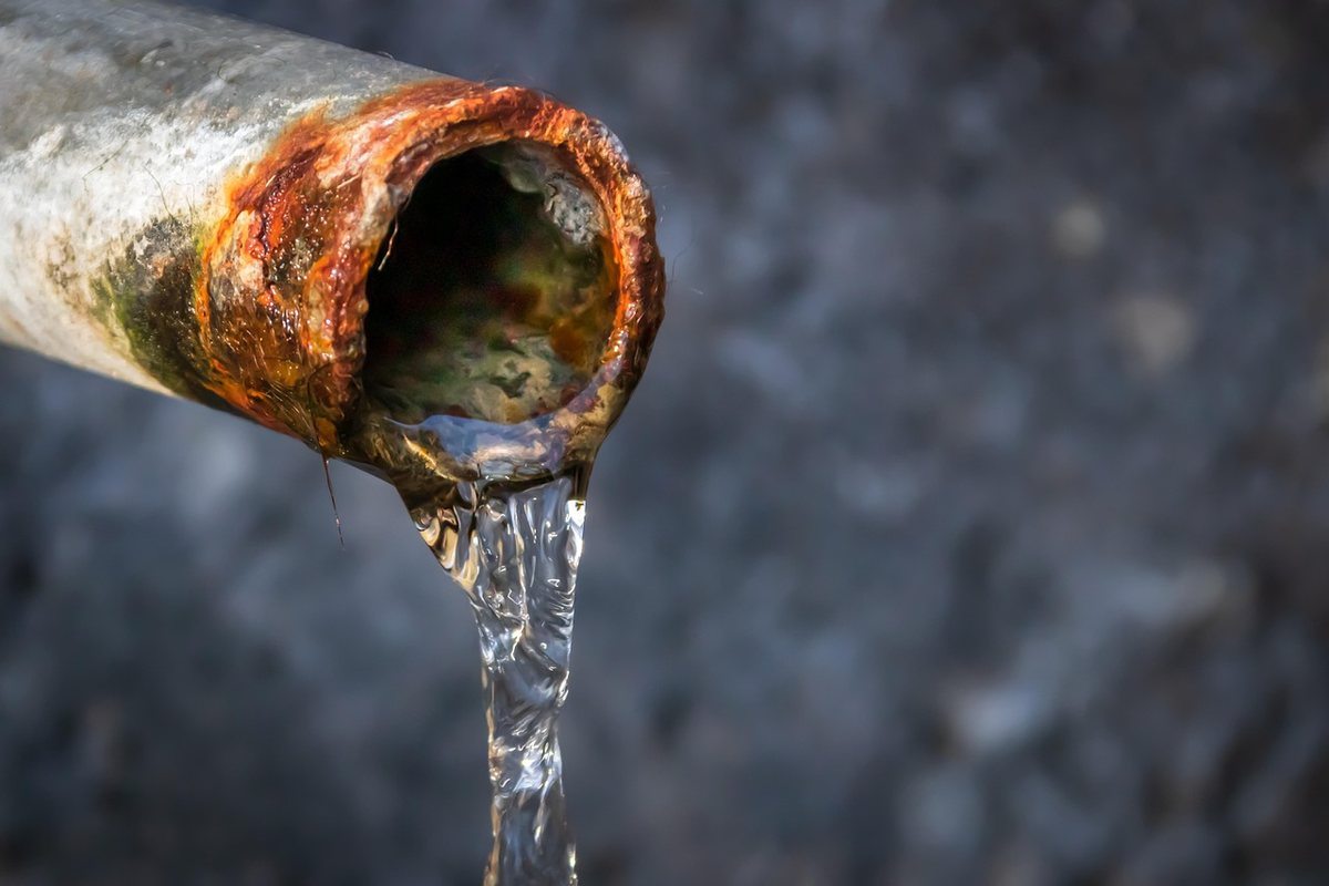 Eau sortant d'un tuyau rouillé sur un fond gris Eau sortant d'un tuyau rouillé sur un fond gris