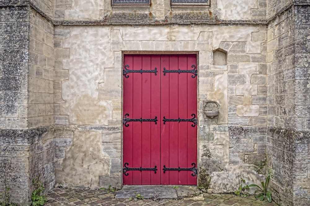 Porte rouge à panneaux encadrée de pierre ancienne sol en pavés
