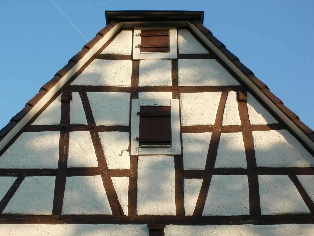 Gros plan sur façade à colombages bois et pans blancs, avec petite fenêtre centrale